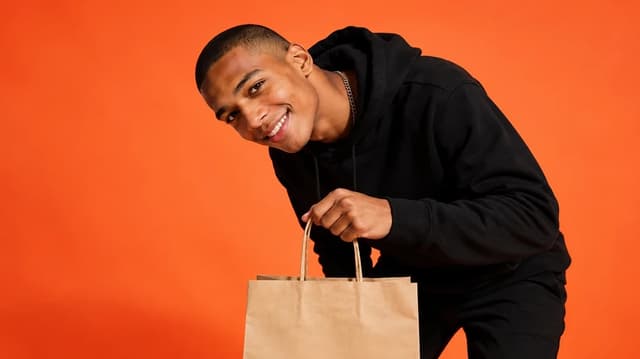 Smiling Runway rider holding a delivery bag against an orange backdrop